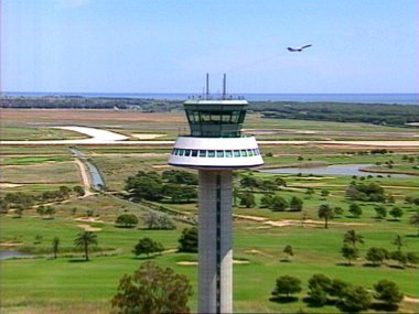 Imatge aèria de la nova torre de control olímpica, el Reial Club de Golf i un avió enlairant-se per la transversal